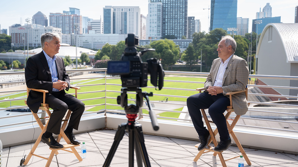 Emory President Gregory Fenves and Georgia Tech President Angel Cabrera in director's chairs with the Midtown Atlanta skyline in the background and a video camera in the foreground. (Photo: Allison Carter)