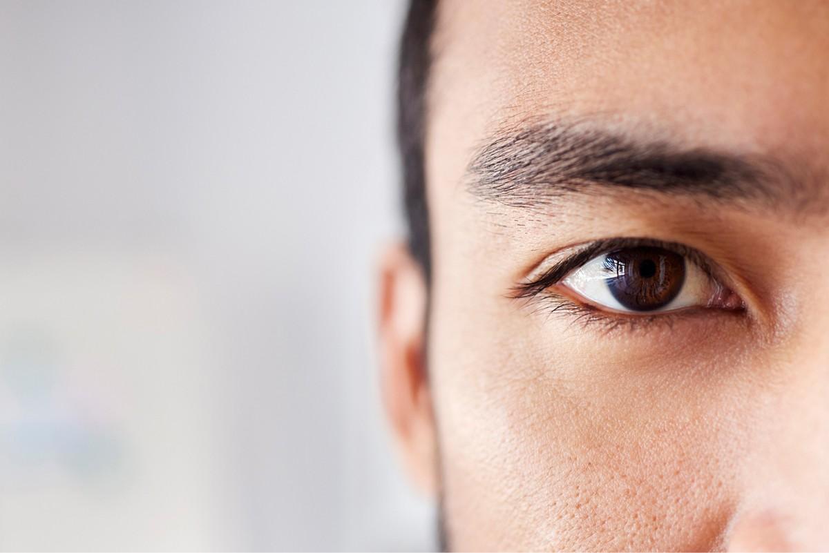 close up of man's brown eye. His dark eyebrows, dark hair, and ear are visible