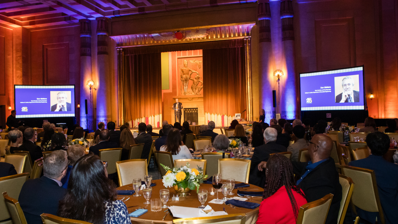 Photo of the Egyptian Ballroom at the Fox Theatre Atlanta looking toward the stage. In the foreground are people sitting in banquet chairs at tables looking at the speaker. In the background is the stage and speaker.